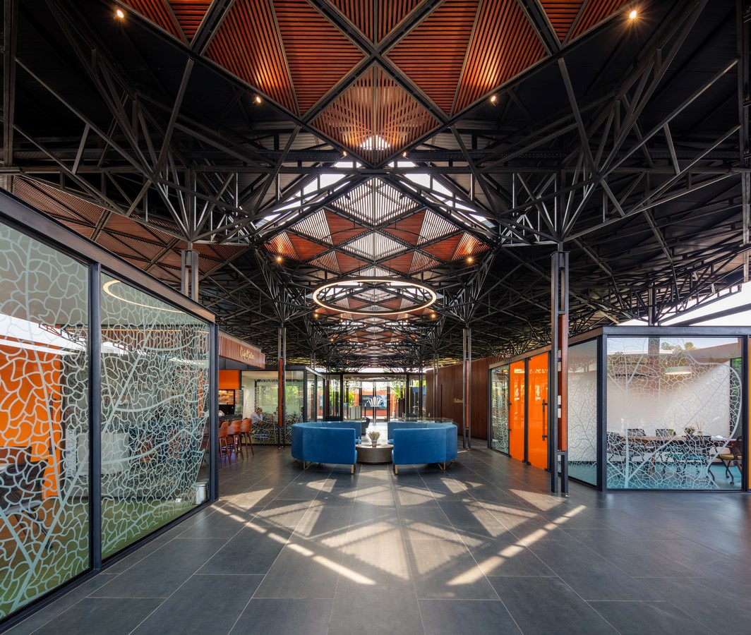PROJECT INFORMATION Project Name: Experience Centre Location: Koyembedu, Chennai Site Area: 0.75 Acre Built-up Area: 0.20 Lac sft No of Floors: 1 Status: Completed Year of Completion:2021 Firm: CnT Architects Design Team (CnT): Amit Rastogi, Karthik P Nair, Anupama Rao Consultants: Metal Queen (Structure), Mukund Associates (Plumbing), Lite Lab (Lighting Design), Oikos (Landscape), Graphics Beyond (Graphic Design) Photography: Andre Fanthome INTRO (470 Words) Located in Chennai metropolitan at a close proximity to city’s transit hub, the site is approached from a highly buzzing Poonamalli high road. Three key components- A marketing office, an Experience centre and a Construction site office are the core of the facility. ‘‘Journey through the project reveals intricately detailed spatial sequences carefully crafted by the thoughtful blend of Architecture, Landscape and Interior design. Visual frames and experiences unfold in layers to keep the visitor captivated & intrigued throughout.’’ A landscaped plaza creating a tranquil arrival experience is first on the entry sequence; doubling up as the interface between city and the main program filtering the unwanted external buzz. At point of arrival, one gets a glimpse of Intricate roof canopy of marketing office hovering over plaza feature wall, creating a sense of mystery for what lies ahead. ‘Marketing office’ is accessed through a curved alley; meandering through lush green it guides visitors to an arrival court revealing full view of the architecture. The form; conceived as an expansive canopy floating over slender metal columns shelters many pods beneath to hold the programme. Pods contain air-conditioned spaces for the reception, gallery, media room, customer studios etc. Arranged in a free plan form, their placement defines a natural movement spine along the longitudinal axis. Intricate design of ceiling and series of skylights along the spine enriches the experience of moving through the space. The ‘Experience centre’ is accessed through a landscape buffer placed at the end of marketing office. Steps through the landscape graduate to a scaled down movement spine representing the proportions of an apartment lobby, leading to three model apartment prototypes put on display here. Placement of model apartments is juxtaposed with various semi open and open public spaces to create a very engaging and enthralling environment. Overall visitor journey is designed as two-way experience and design features are tactfully placed along the path and at important nodes to be discovered gradually and slowly. A discreetly placed entryway at the end of experience centre leads in to the ‘Construction site office’. Encouraged to see the importance given to design of spaces for the construction team; visitors are escorted right through the common area of site office arriving on to a viewing deck opening to a panoramic view of the under construction residential township which is rising up in the background. Environmental impact: Life span of facility is five years, post which it will be dismantled. Hence, majority of the structure is designed in steel for recyclability and reuse. The modular structural elements are going to be used for another project of the developer, making this project as sustainable as possible. Circulation spaces are well shaded and allow a lot of cross breezes, essential for comfort in hot humid weather of Chennai; reducing need of air conditioning to the minimum. - Sheet10